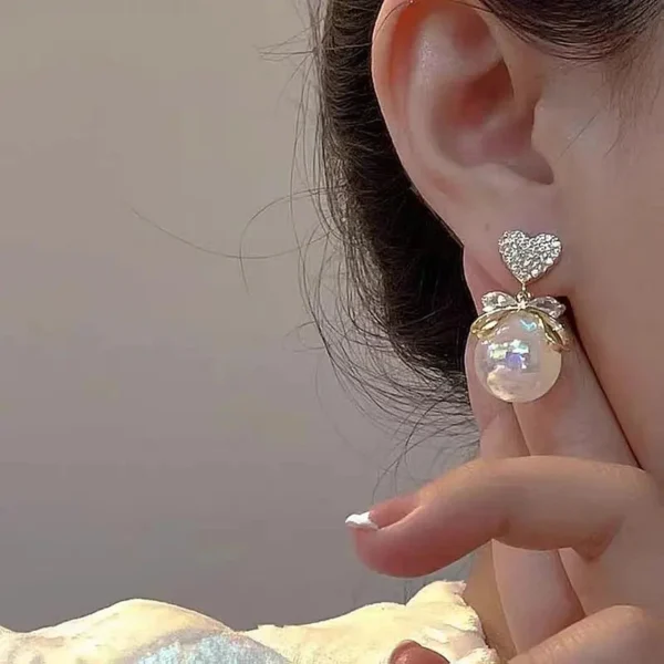 Model wearing romantic pearl drop earrings with heart stud
