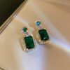 "Elegant emerald green drop earrings with rectangular and round stones bordered by diamond accents on gold plating"