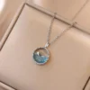 Elegant silver pendant featuring a 3D whale swimming over a sparkling ocean-blue crystal, displayed on a soft beige jewelry box.
