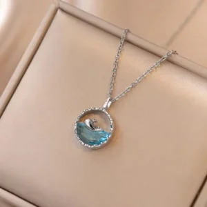 Elegant silver pendant featuring a 3D whale swimming over a sparkling ocean-blue crystal, displayed on a soft beige jewelry box.
