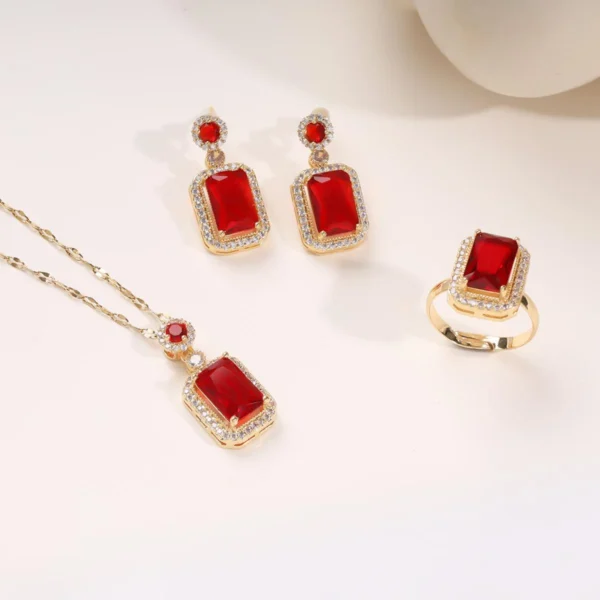 Gold jewelry set with red rectangular stones and diamond accents, including a necklace, earrings, and ring on a cream background.