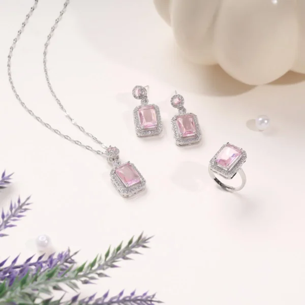 Elegant pink gemstone jewelry set with necklace, earrings, and ring in silver-tone setting, styled on a pastel backdrop.