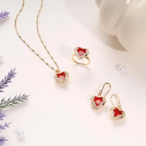 Gorgeous 3-piece gold jewelry set with red heart-shaped stones, including a necklace, ring, and earrings, adorned with sparkling crystals, displayed elegantly on a cream background.