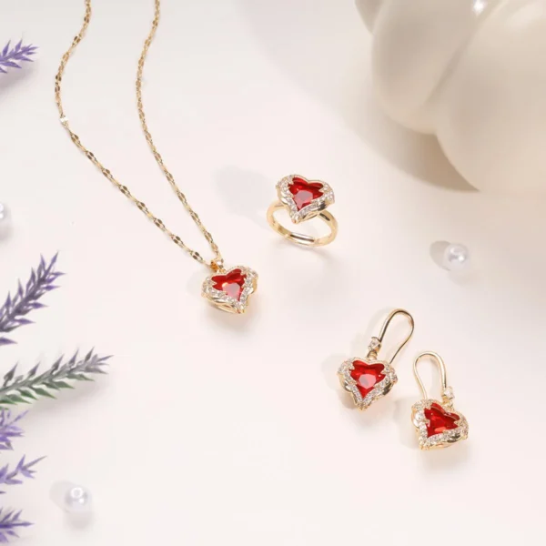 Gorgeous 3-piece gold jewelry set with red heart-shaped stones, including a necklace, ring, and earrings, adorned with sparkling crystals, displayed elegantly on a cream background.