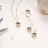 Elegant silver jewelry set featuring a green heart-shaped gemstone necklace, matching earrings, and a ring, all adorned with sparkling white stones, styled on a minimal light background.
