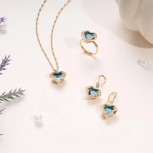 Elegant silver jewelry set featuring a green heart-shaped gemstone necklace, matching earrings, and a ring, all adorned with sparkling white stones, styled on a minimal light background.