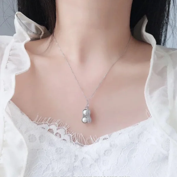 Silver necklace with a peanut-shaped pendant featuring twin pearls inside a textured metallic shell design