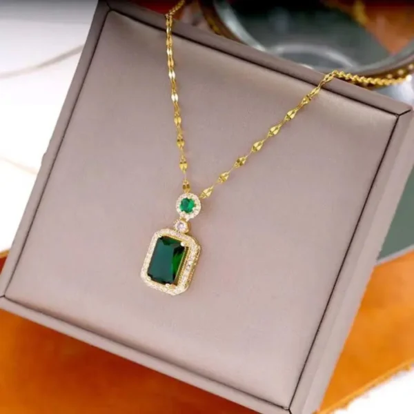 Gold chain necklace with rectangular green gemstone pendant surrounded by diamonds, displayed on a box.
