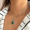 A woman wearing a glamorous emerald-cut green stone necklace with a sparkling halo setting on a delicate silver chain.