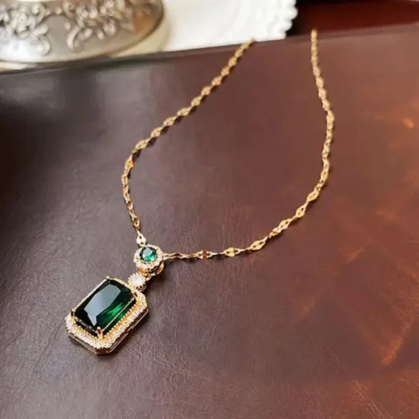 Gold chain necklace with rectangular green gemstone pendant surrounded by diamonds, displayed on a box.