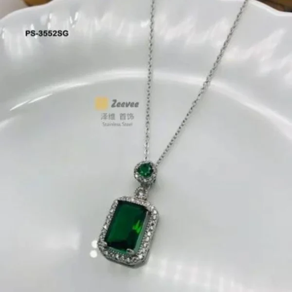 A woman wearing a glamorous emerald-cut green stone necklace with a sparkling halo setting on a delicate silver chain.