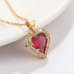 Gold chain necklace with a sparkling red heart-shaped gemstone pendant outlined with white crystals, styled on a white background.