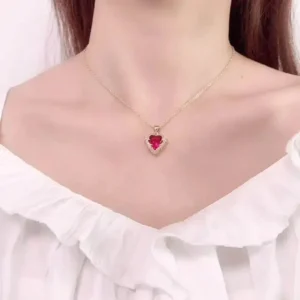 Gold chain necklace with a sparkling red heart-shaped gemstone pendant outlined with white crystals, styled on a white background.