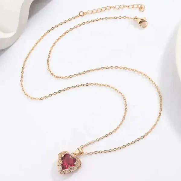 Gold chain necklace with a sparkling red heart-shaped gemstone pendant outlined with white crystals, styled on a white background.