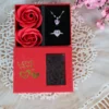 Red “LOVE” gift box with pink heart necklace and ring set, alongside two artificial red roses and a transparent display window.