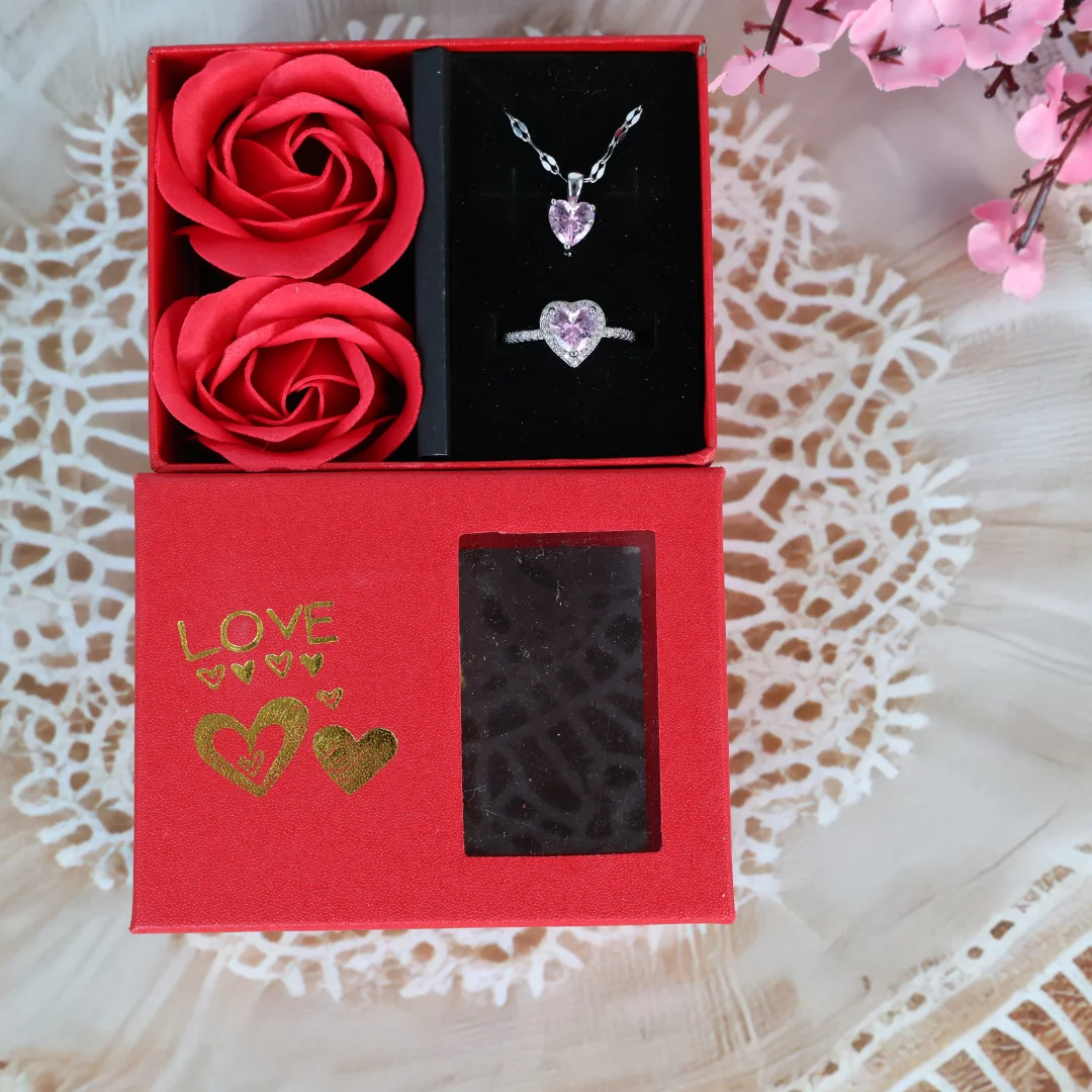 Red “LOVE” gift box with pink heart necklace and ring set, alongside two artificial red roses and a transparent display window.
