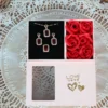 Pink gift box with ruby red jewelry set (necklace, earrings, ring) and artificial red roses arranged inside.
