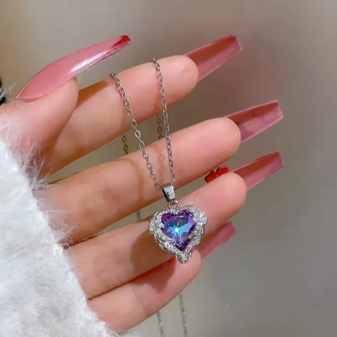 Elegant silver chain necklace with a radiant deep blue heart-shaped gemstone pendant, surrounded by shimmering white crystals, resting on a silky white fabric background.