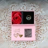 Gold dolphin ring with blue crystal in a pink gift box and red rose on lace background.