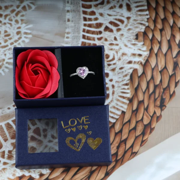 Navy blue gift box with pink heart-shaped ring and a red artificial rose, gold "LOVE" print on the lid.