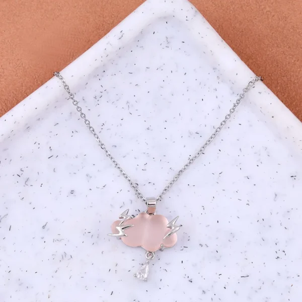 Silver chain necklace with a light pink cloud-shaped pendant, lightning bolt accents, and a teardrop crystal charm, displayed on a terrazzo-style surface.
