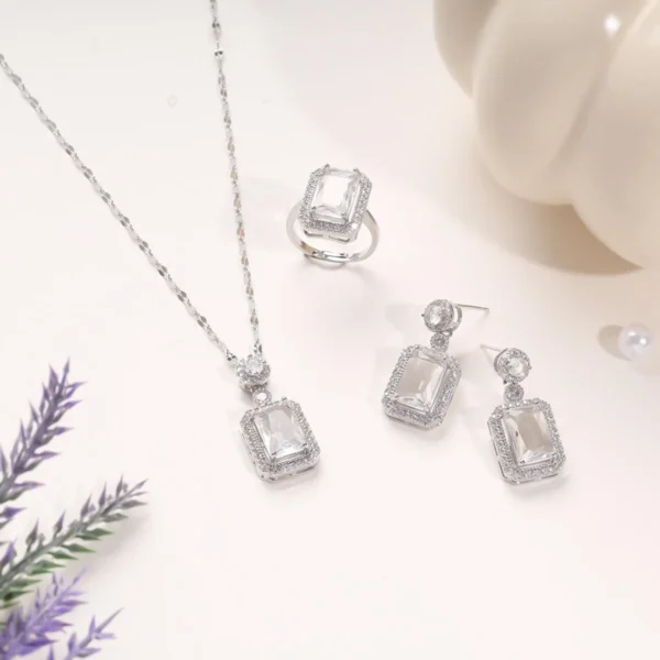 Elegant silver jewelry set featuring a necklace, ring, and earrings with rectangular crystal stones on a soft cream background.