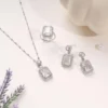 Elegant silver jewelry set featuring a necklace, ring, and earrings with rectangular crystal stones on a soft cream background.