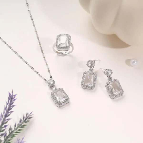 Elegant silver jewelry set featuring a necklace, ring, and earrings with rectangular crystal stones on a soft cream background.