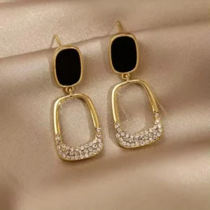 Black and gold rectangular drop earrings with crystal stone detailing on satin background