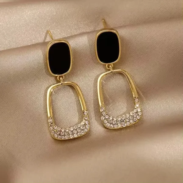 Black and gold rectangular drop earrings with crystal stone detailing on satin background