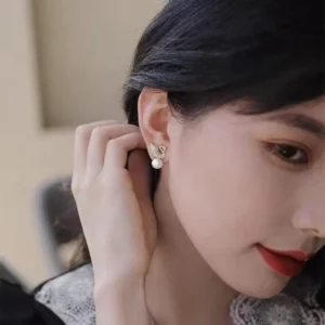 Gold swan-shaped earrings with white pearl drop and crystal detailing on satin fabric