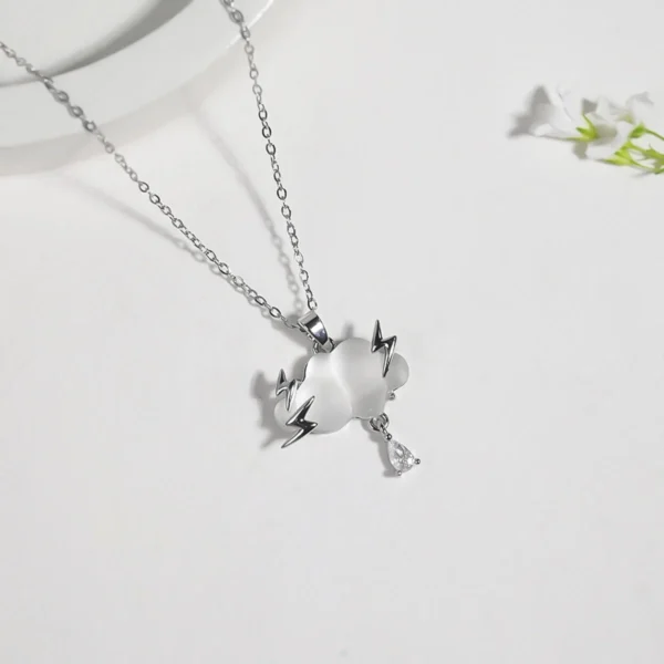 Gold chain necklace featuring a frosted white cloud pendant with lightning bolt details and a teardrop charm, styled with natural stones and wood.