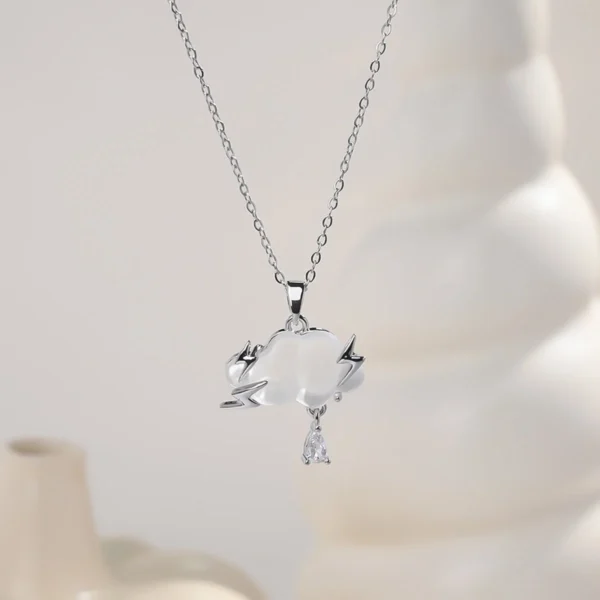 Gold chain necklace featuring a frosted white cloud pendant with lightning bolt details and a teardrop charm, styled with natural stones and wood.